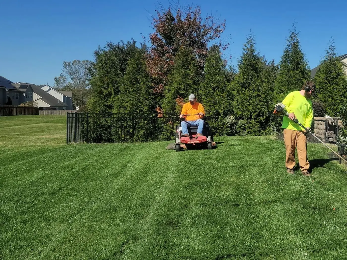 A lawn care crew mowing with a zero-turn and trimming a striped lawn